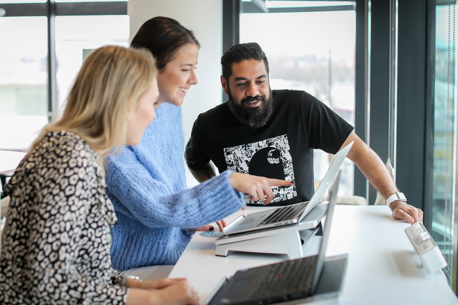 Three people standing at a desk in an office looking at a laptop screen