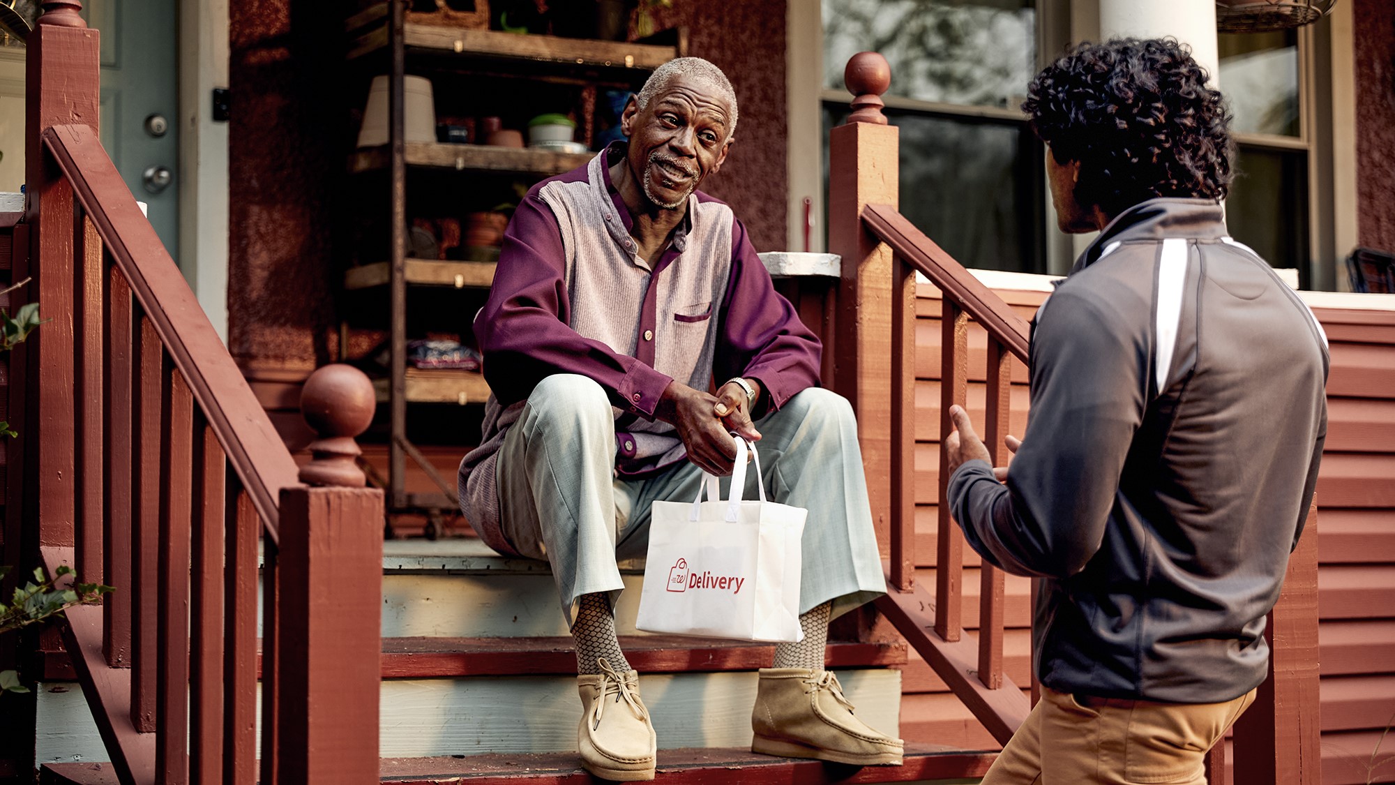 Older man on his front porch receiving a 1-hour delivery bag from a Walgreens team member