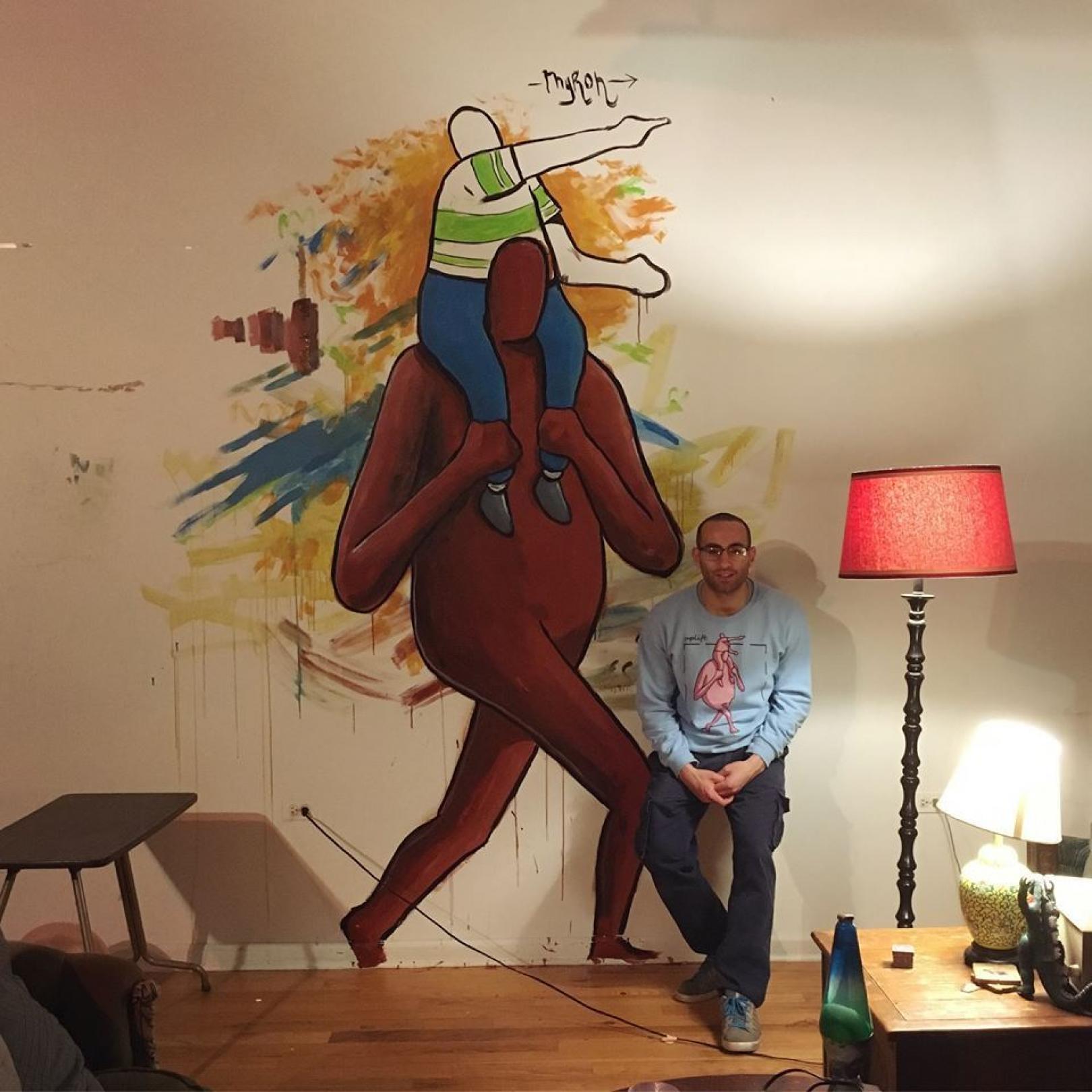 Myron sitting next to the mural in his house