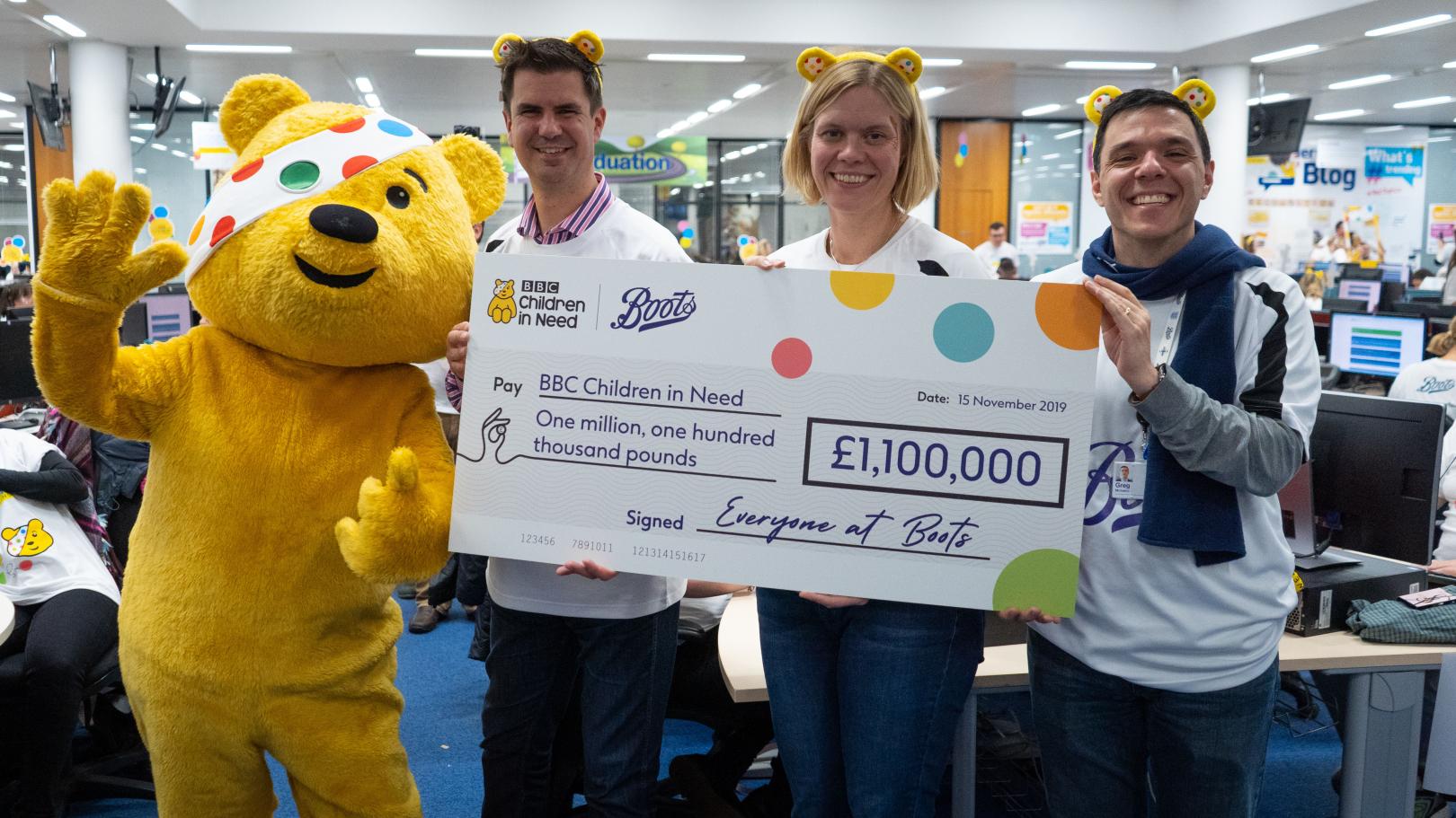 Three team members and the Children in Need Pudsey bear holding a large board showing how much money was raised.