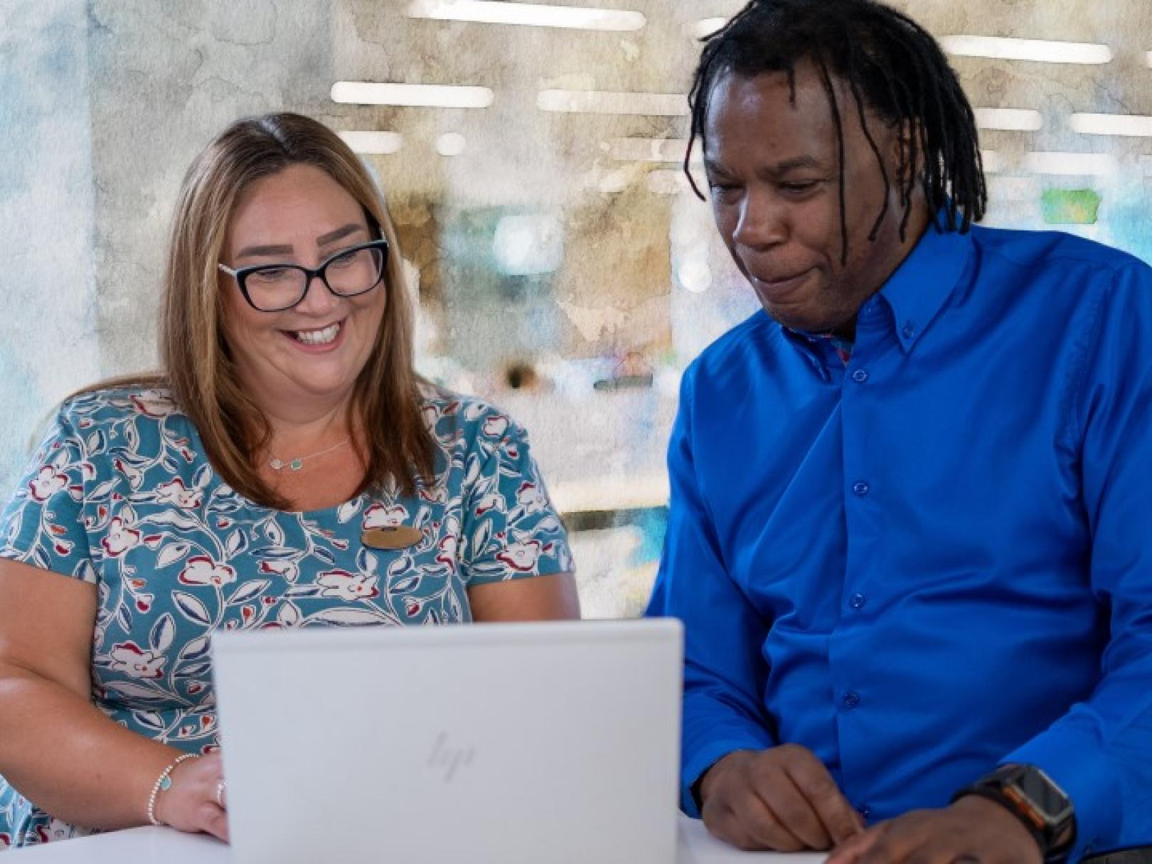 White woman and black man looking at a laptop together in an office