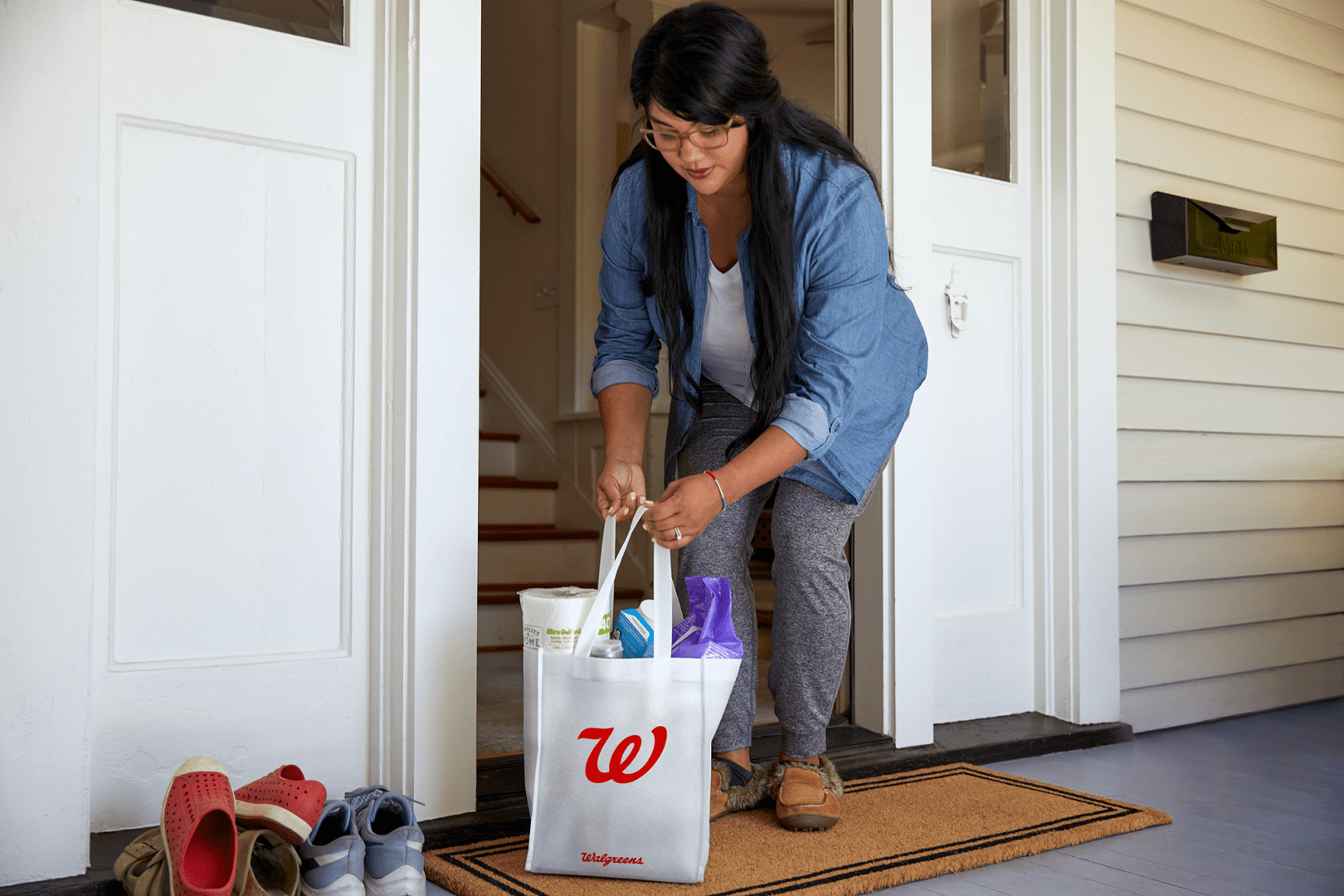 Woman picking up Walgreens bag from porch