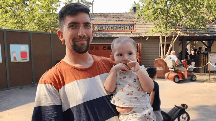A man holding his two-year-old daughter at a park.