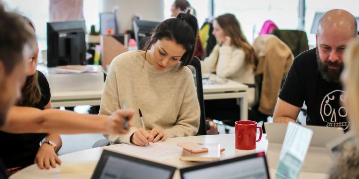 Colleagues sitting at a desk in an open plan office having a meeting