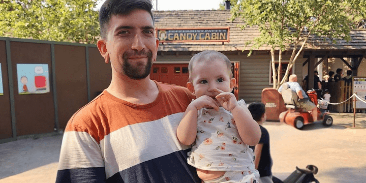A man holding his two-year-old daughter at a park.